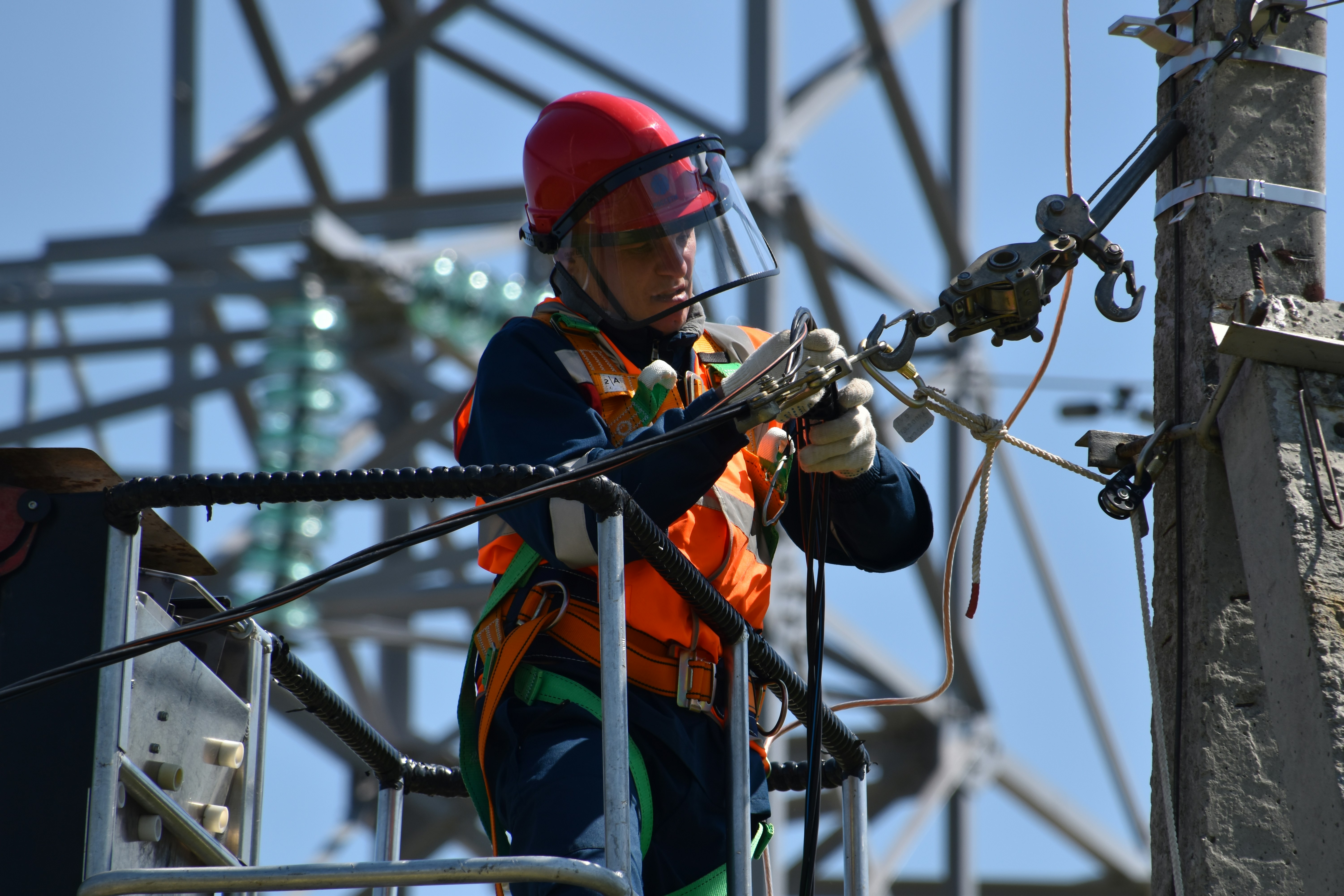 Elektryk w kasku i uprzęży pracujący przy instalacji elektrycznej